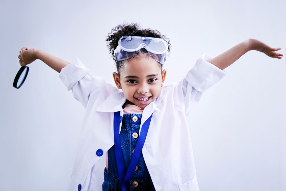 bambina che sorrise vestita con un camice bianco e con in mano una lente di ingrandimento