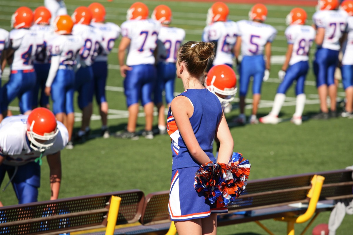 Ragazza cheerleader in uniforme di squadra con il gruppo di football durante una partita