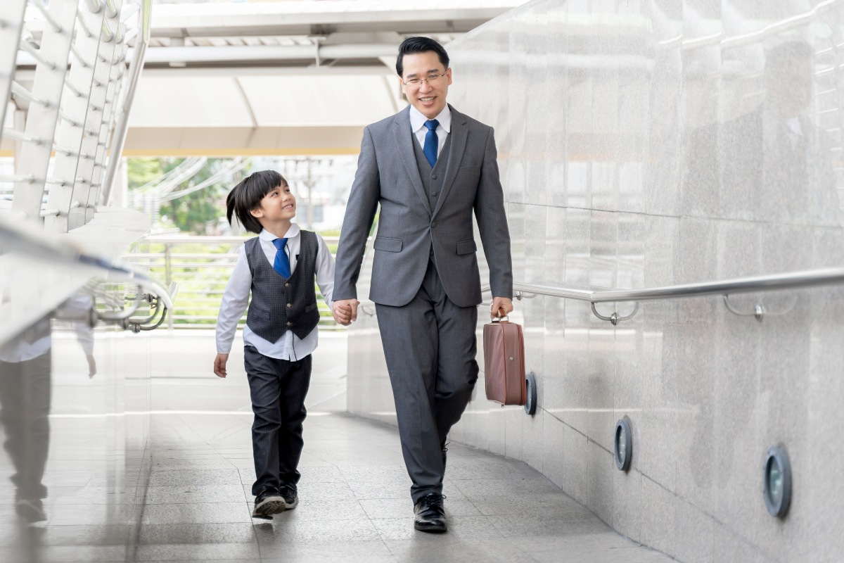 Figlio sorridente tiene la mano del papà mentre lo accompagna in ufficio